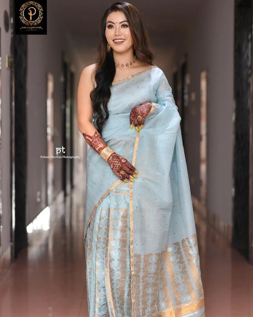 a woman in a blue sari with gold accents on her hands and arms, posing for the camera