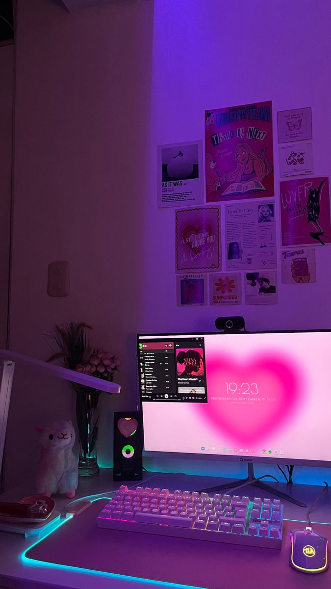 a computer desk with a keyboard, mouse and monitor lit up by neon lights on the wall