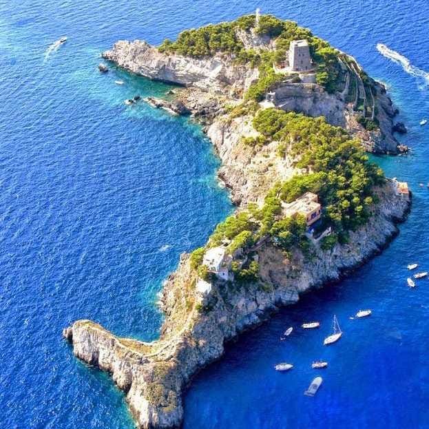 an island in the middle of the ocean with boats floating on it's surface