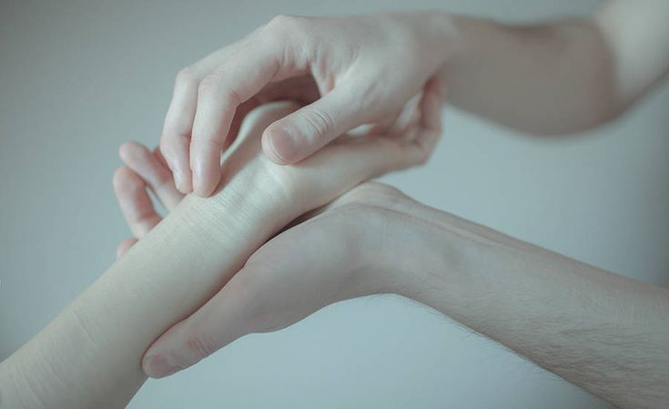 two hands reaching towards each other with one hand on the other's arm, in front of a white background