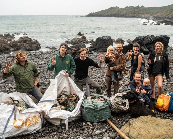 a group of people standing on top of a rocky beach next to the ocean with bags