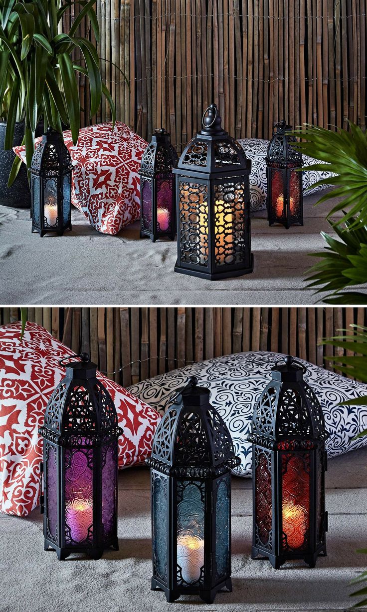 three different lanterns with candles in them sitting on the ground next to pillows and plants