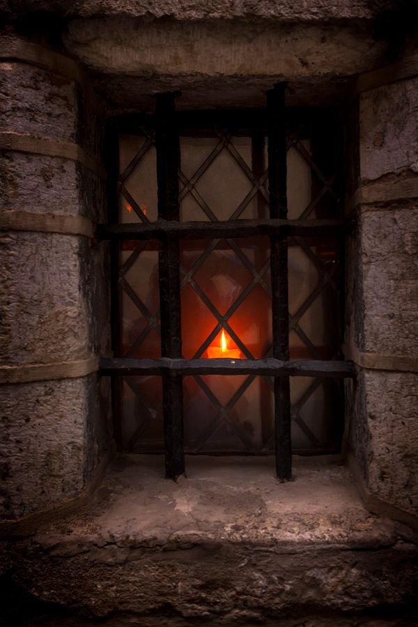 a candle is lit in the window of an old stone building with bars on it