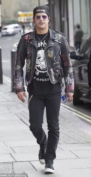 a man walking down the street wearing black pants and a leather jacket with skulls on it