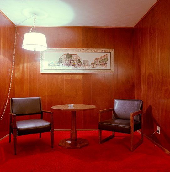 two chairs and a table in a room with wood paneling on the wall behind them