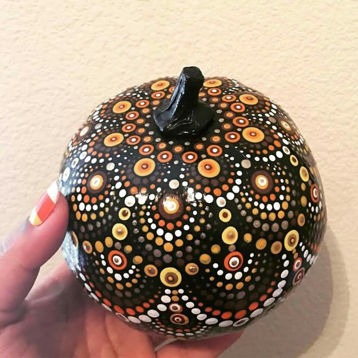 a hand holding a painted pumpkin in the shape of a ball with circles on it