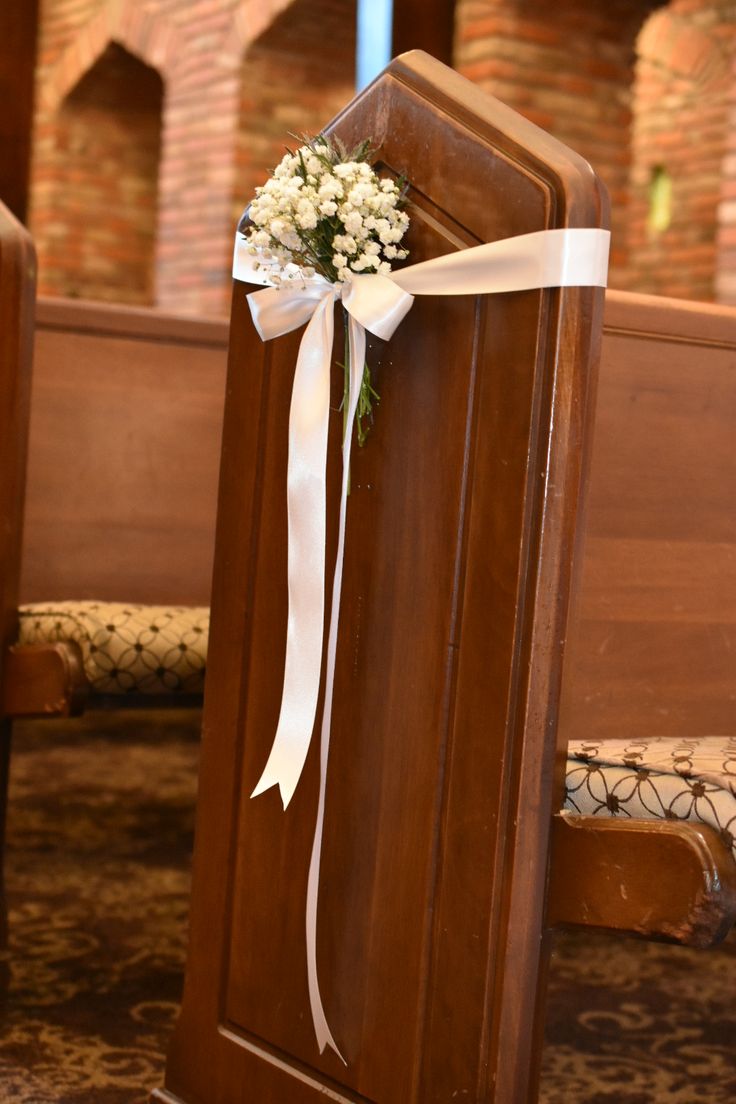 a bouquet of baby's breath sits on the back of a wooden church pew