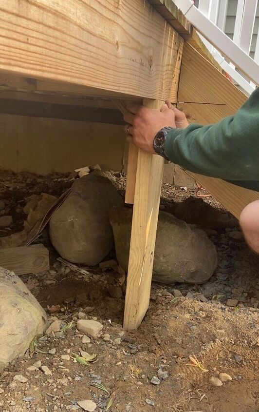 a man is working on the side of a house with rocks and wood under it