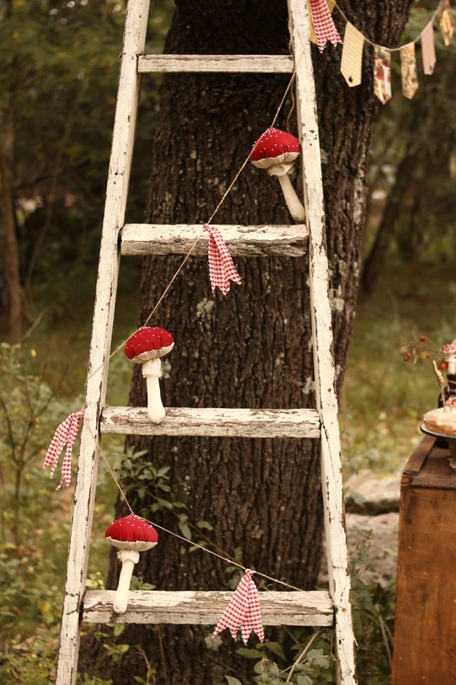 an old wooden ladder is decorated with red and white fabric mushrooms on the tree trunk