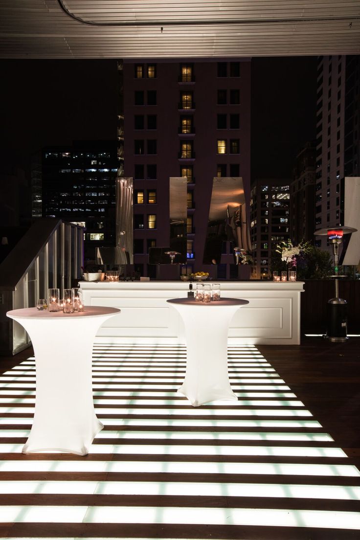 two white tables sitting next to each other on top of a hard wood floor in front of tall buildings