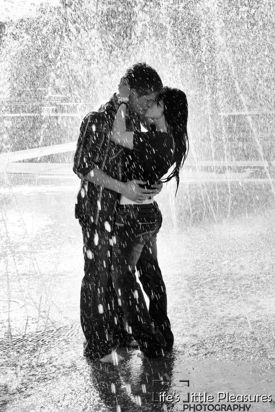 black and white photograph of two people hugging under an umbrella in the rain with water splashing all around them