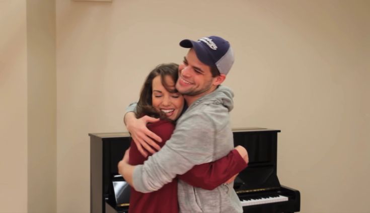 a man and woman hugging each other in front of a piano with their arms around each other