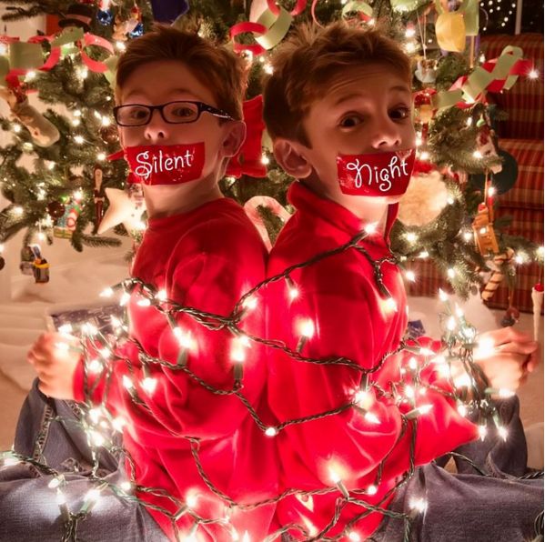 two young boys sitting next to each other in front of a christmas tree with lights