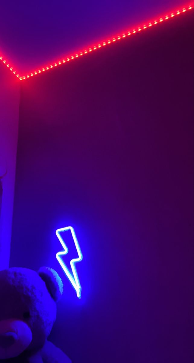 a teddy bear sitting in front of a neon sign with a lightning bolt on it