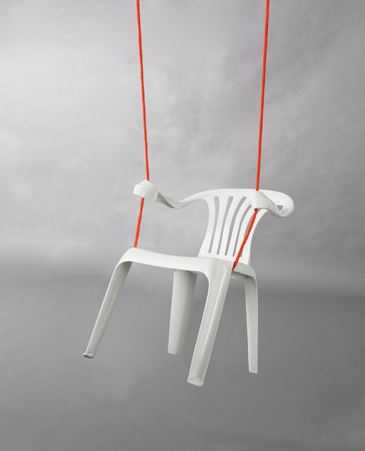 a white plastic chair hanging from a red string on a gray and grey sky background