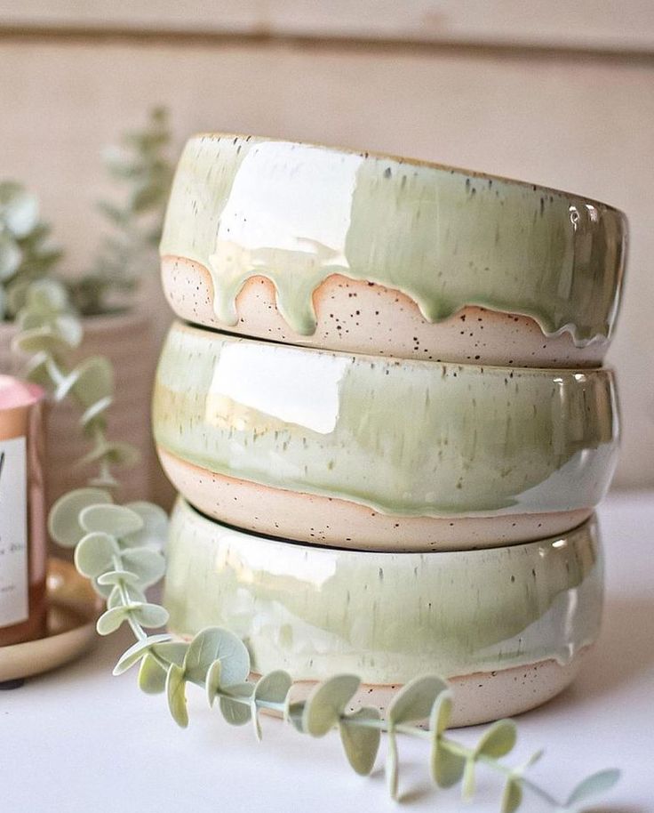 three ceramic bowls are stacked on top of each other next to some plants and a candle