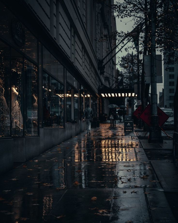 people walking down the street on a rainy night with umbrellas in the foreground