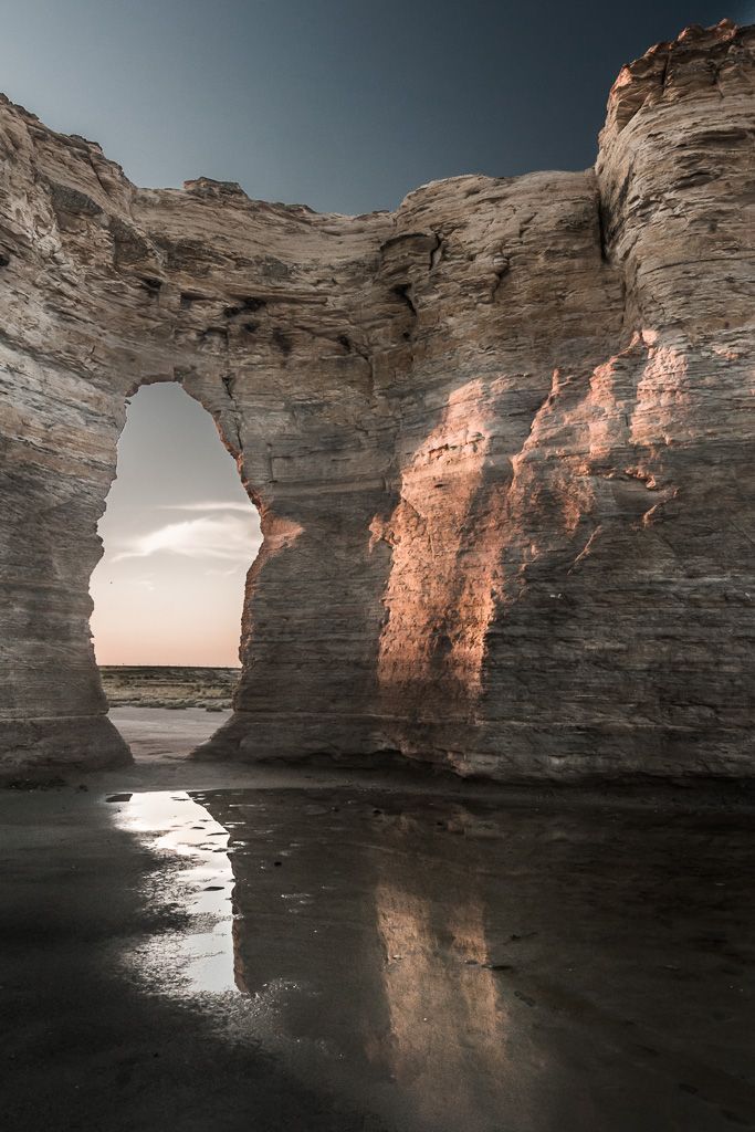 the sun is shining through an arch in the rock formation on the beach at low tide