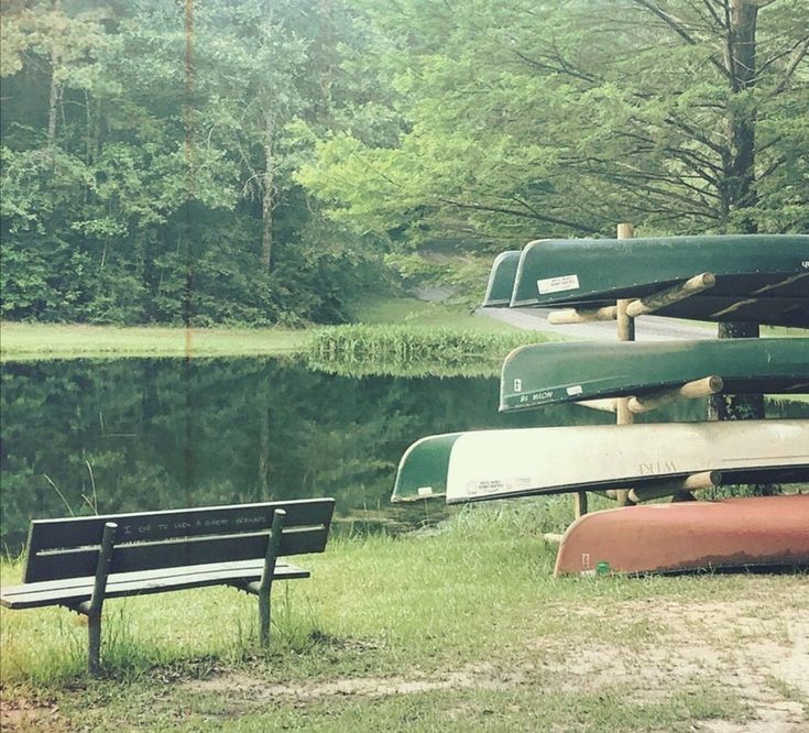 several canoes are stacked on top of each other near a bench by the water