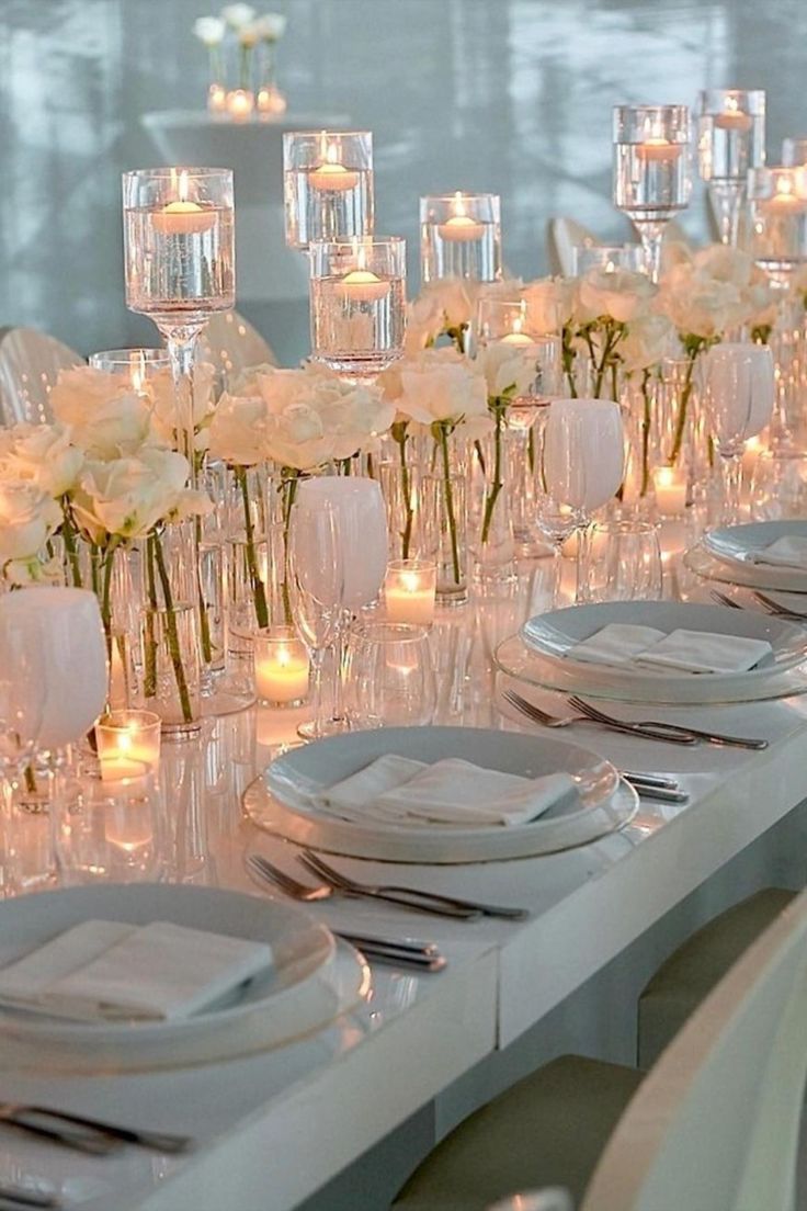 a long table is set with white flowers and place settings for dinner guests to enjoy