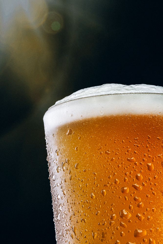 a close up of a beer glass with water droplets on the surface and sun shining in the background