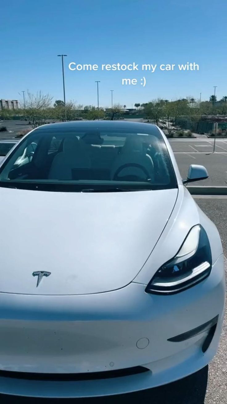 a white tesla parked in a parking lot with the words come re stock my car with me