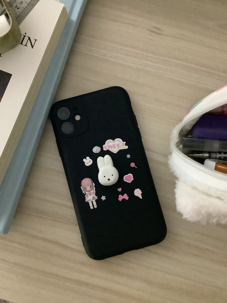 a black phone case with an animal sticker on it sitting next to a book