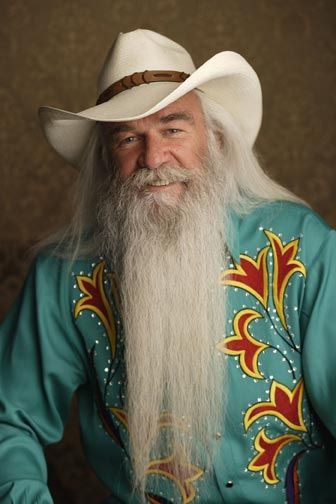 an old man with a long white beard wearing a cowboy hat and blue shirt is posing for the camera