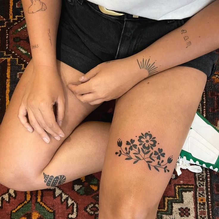 a woman sitting on the floor with her legs crossed and tattoos on her leg,