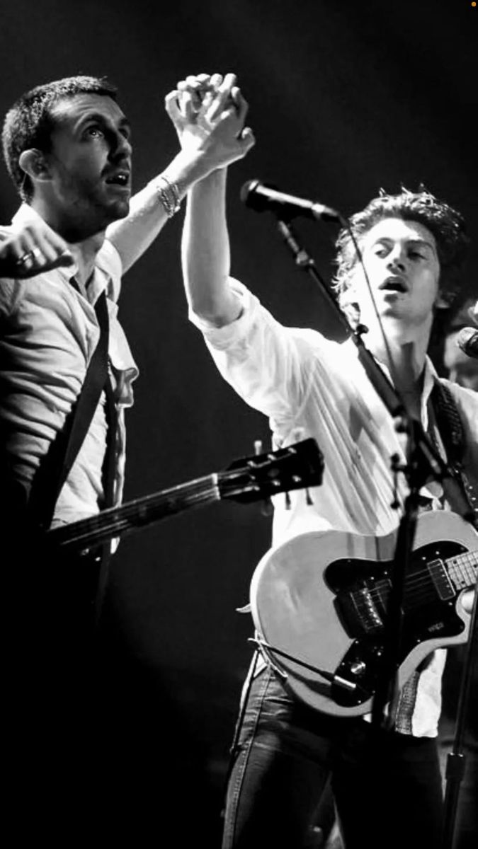 two young men singing into microphones while one holds his hand up to the sky