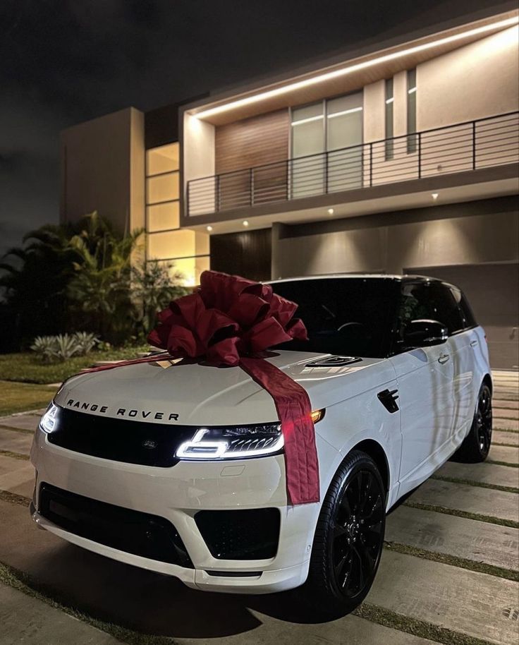 a white range rover with a red bow on it's hood parked in front of a house