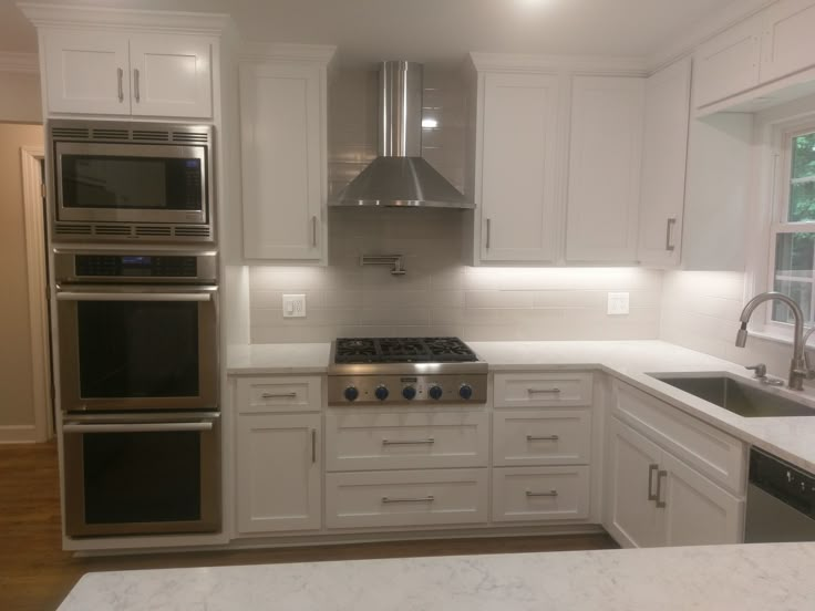 a white kitchen with stainless steel appliances and marble counter tops, along with an island in the middle