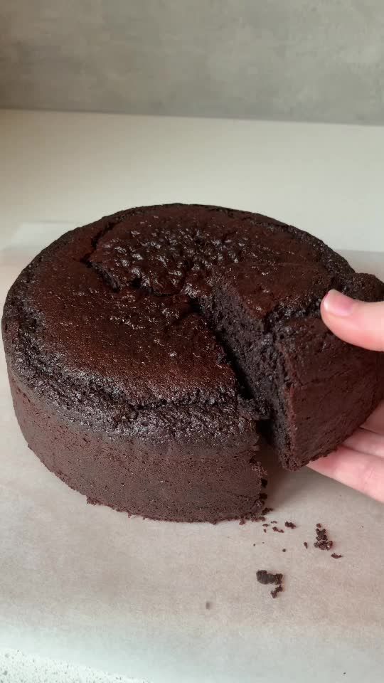 a person holding a piece of chocolate cake in front of the other half of it