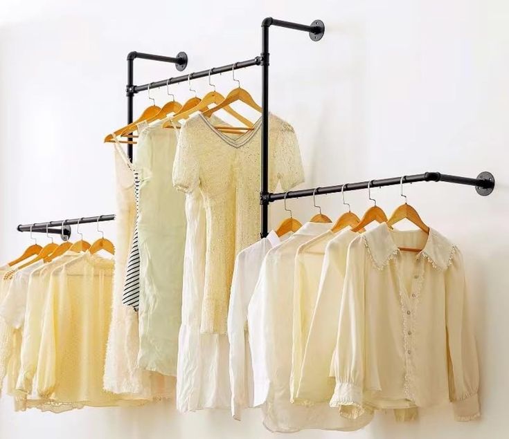 there are many shirts hanging on the clothes rack in front of the wall and one is yellow