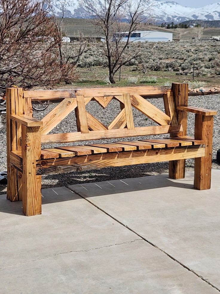 a wooden bench sitting on top of a cement ground next to a tree and bushes