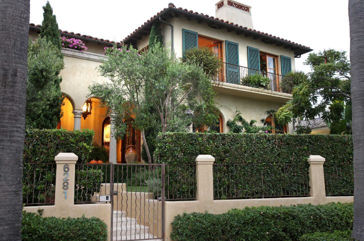 a large house with many windows and bushes in front of it, along with a gated driveway