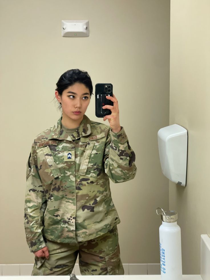 a woman in uniform taking a selfie in the bathroom mirror with her cell phone