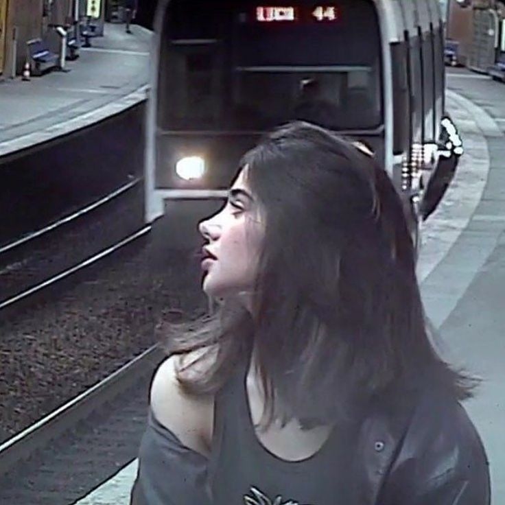 a woman standing in front of a train at a station with her head turned to the side