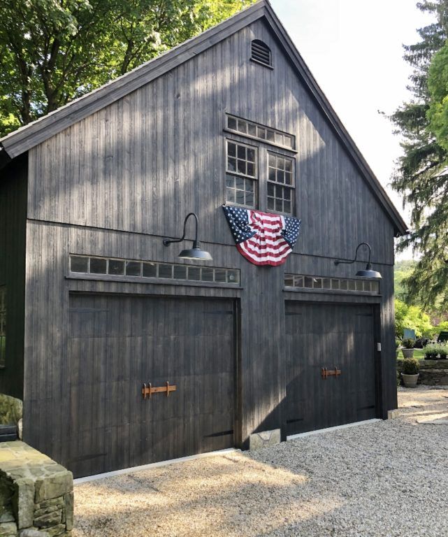 an american flag is hanging on the side of a barn with two garage doors and windows