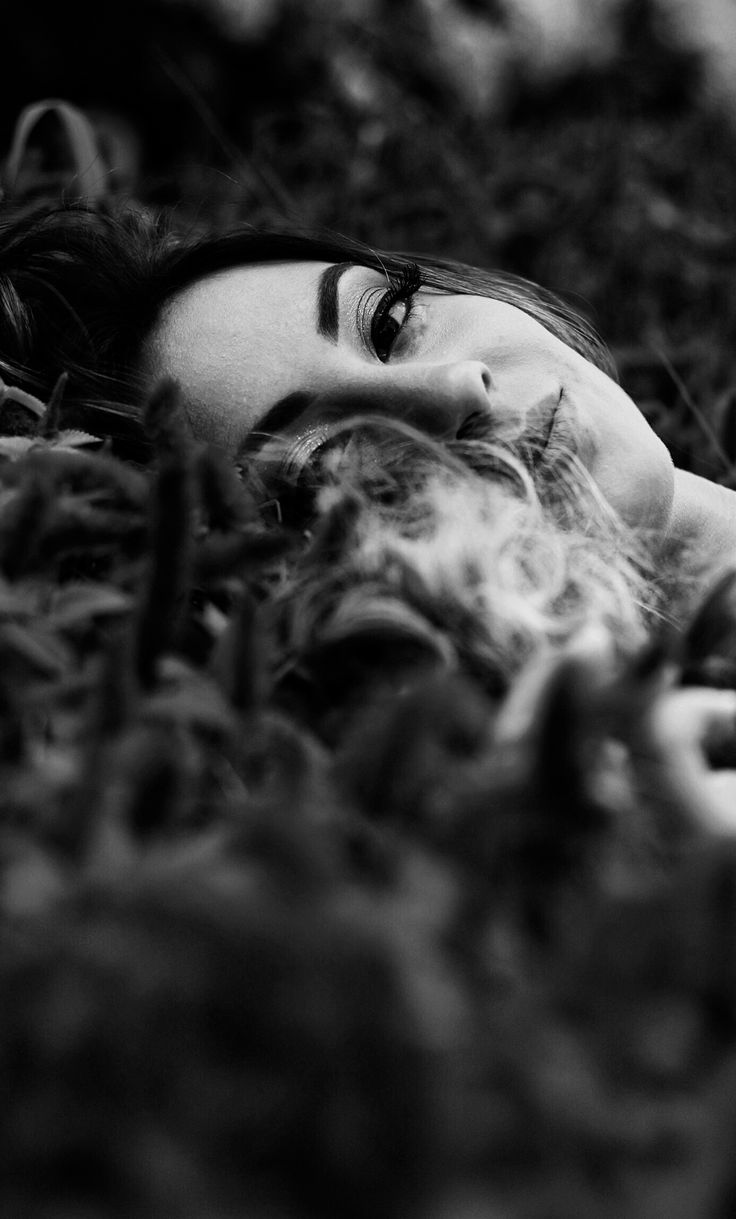 a black and white photo of a woman laying in the grass with her eyes closed