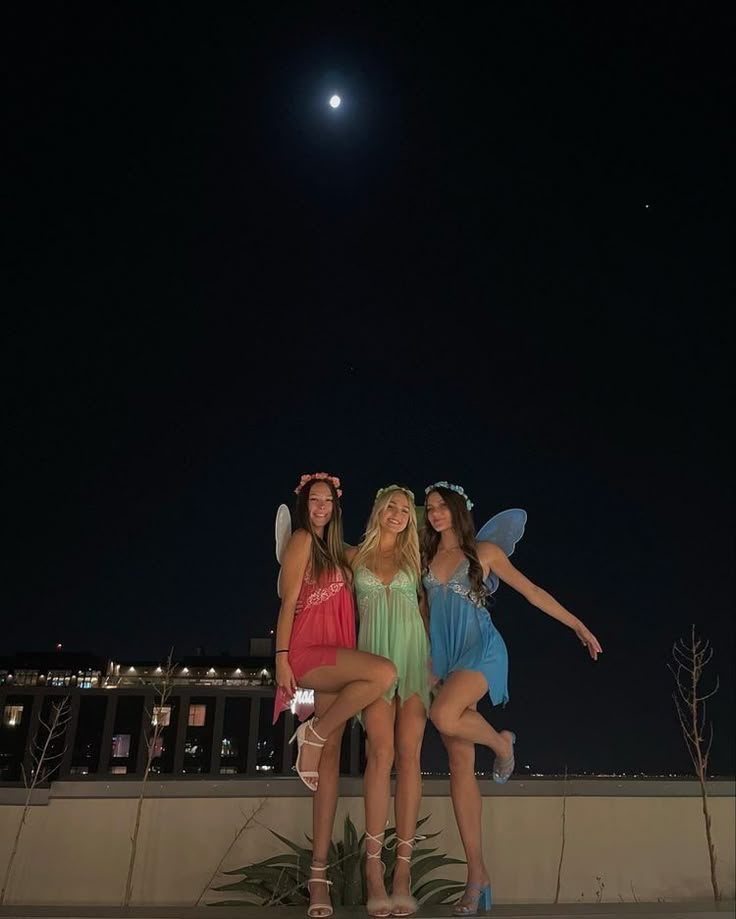 three beautiful young women standing next to each other in front of a building at night