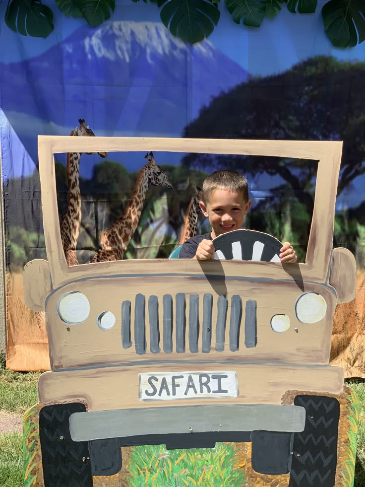 a young boy driving a safari vehicle with giraffes in the back ground