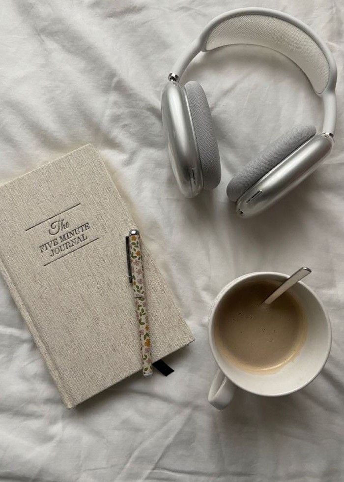 a cup of coffee, headphones and notebook on a bed