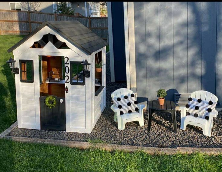 two white chairs sitting in front of a small house