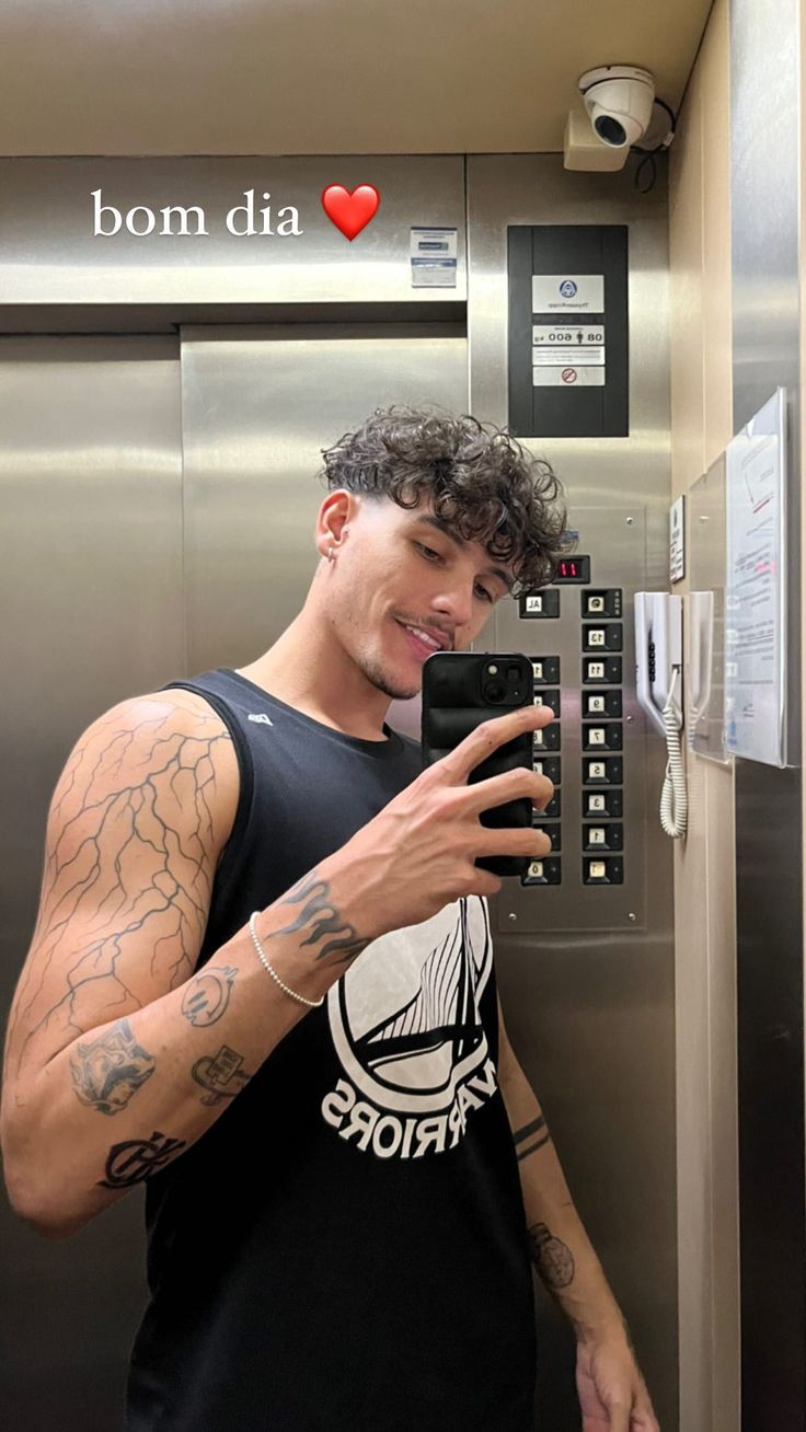 a man with tattoos is looking at his cell phone while standing in front of an elevator