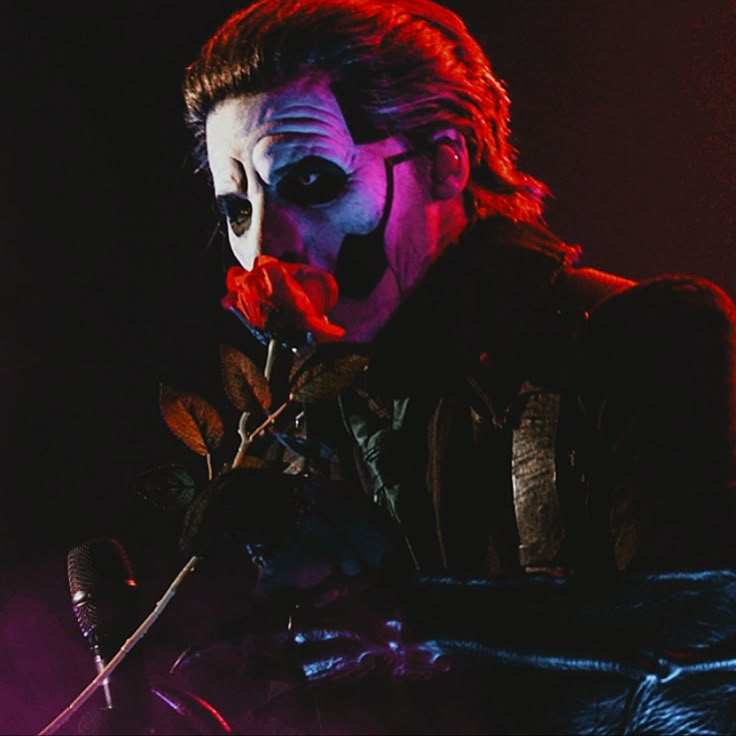 a man with red hair and makeup holding a knife in his hand while wearing a clown mask