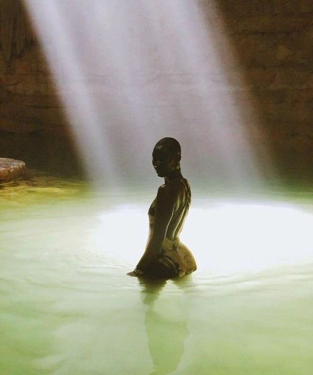 a woman is sitting in the water with her back turned to the camera and light coming from behind