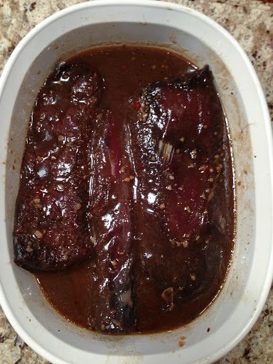 two pieces of meat in a white bowl on top of a granite counter with brown gravy