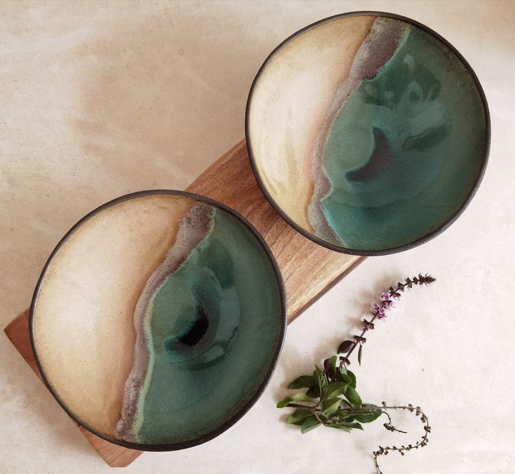 two green and white bowls sitting on top of a wooden board next to a plant