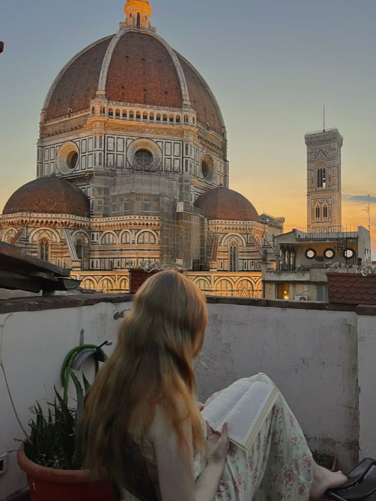 a woman sitting on top of a roof next to a tall building with a dome